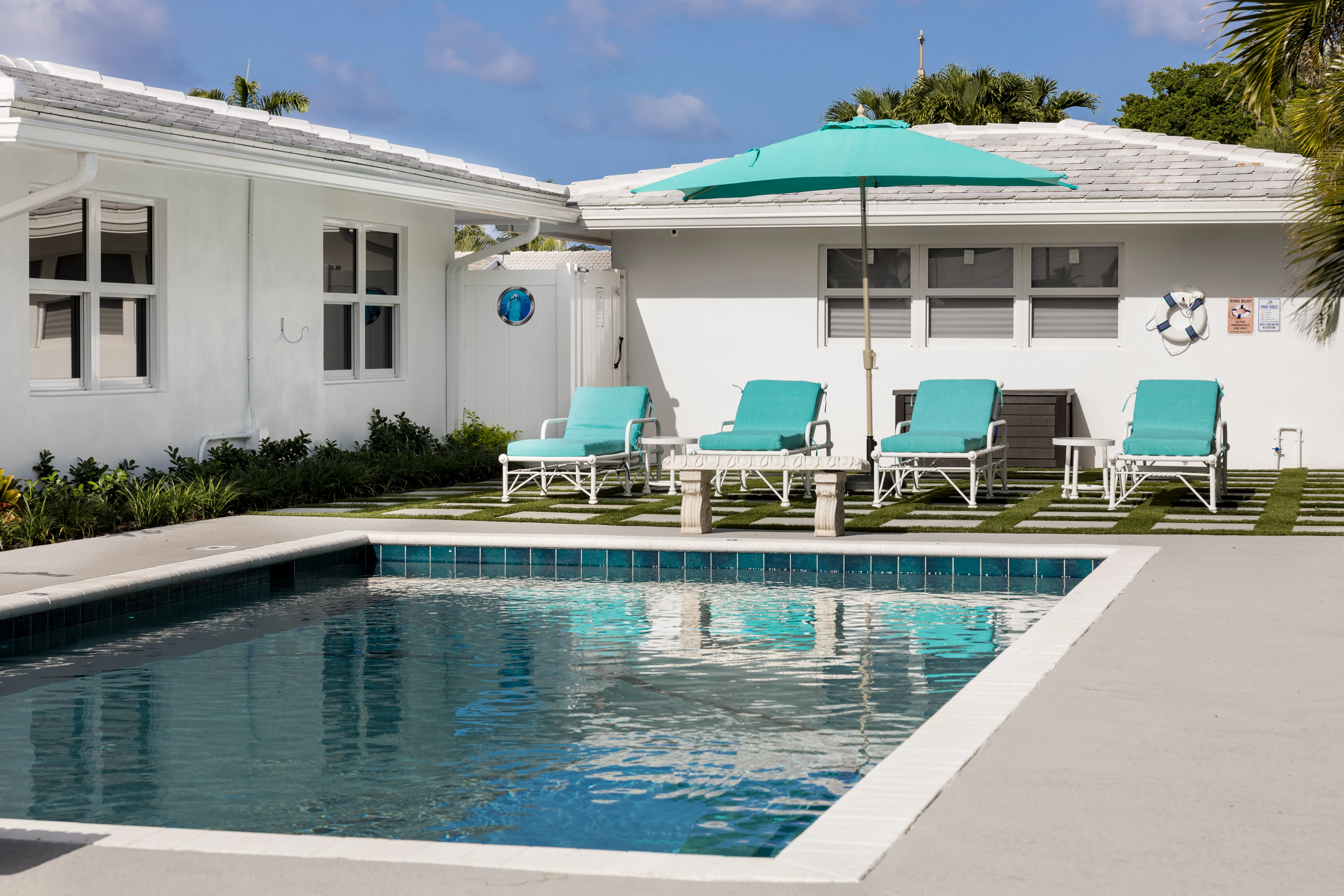 Private residential pool with turquoise lounge chairs and sun umbrella beside white modern house – Dallas Pools Contractor